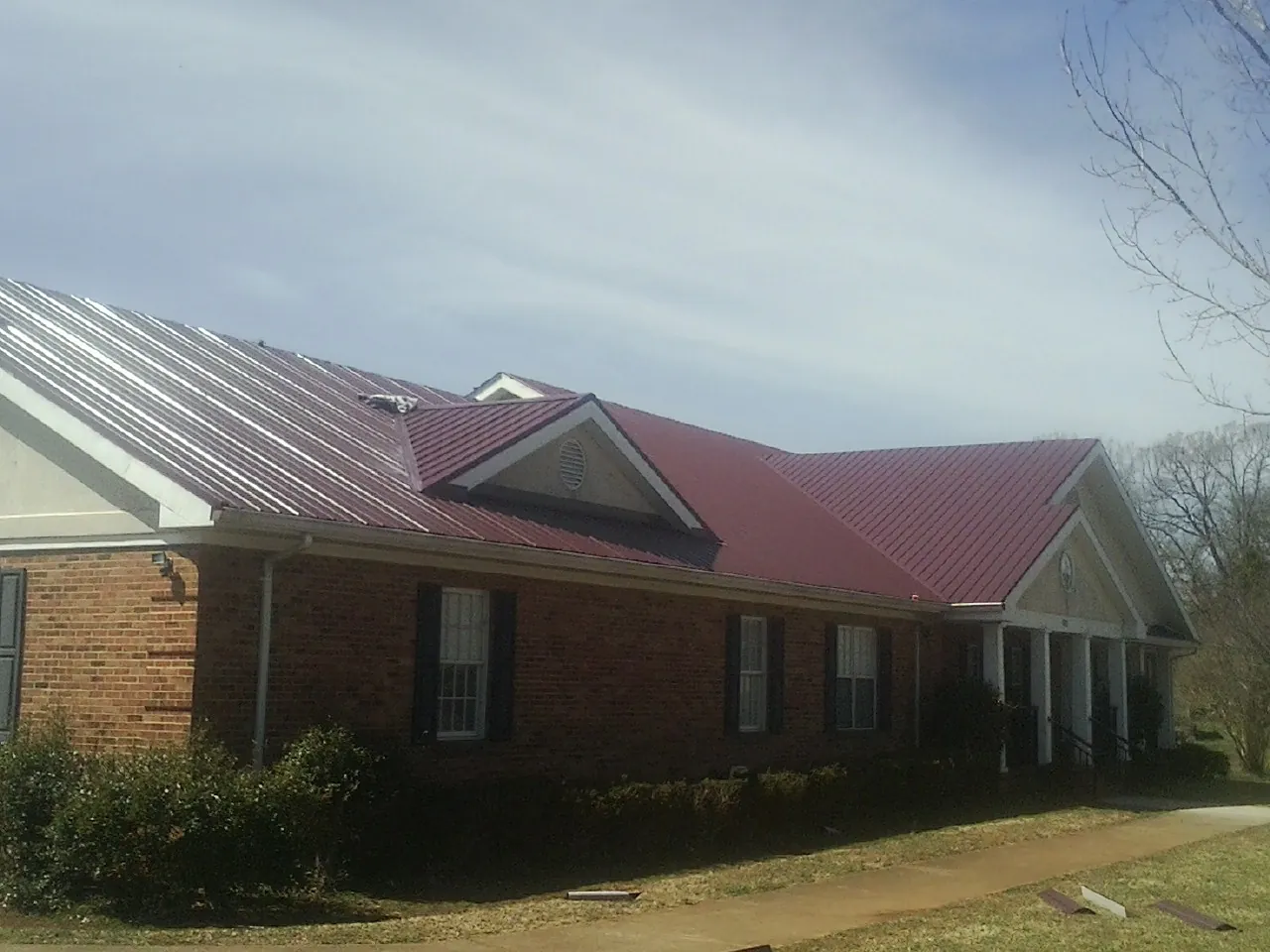 Red metal roof with gabled entries on a long brick building, from a Hail Damage Roof Repair job in El Monte