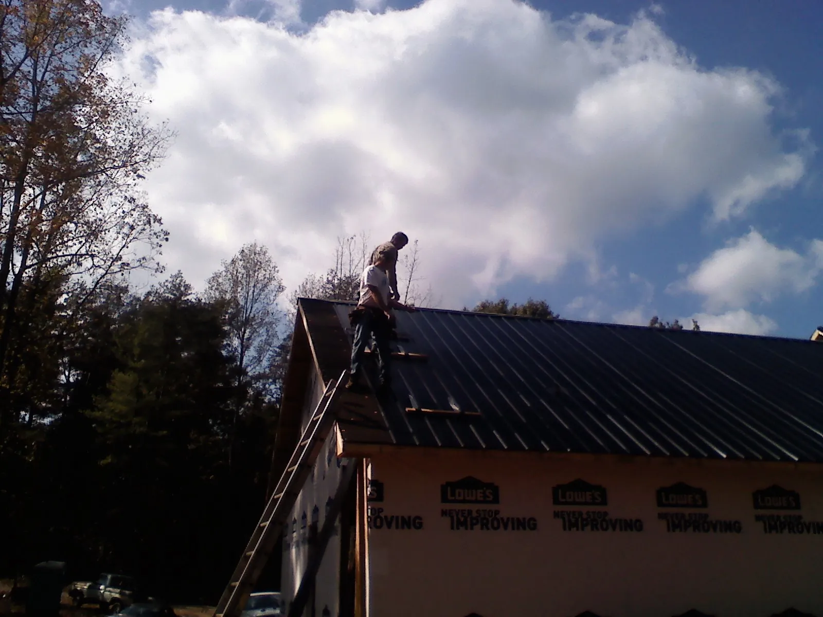 Roofer fastening dark metal panels high against a cloudy sky, from a Roof Inspection job in El Monte
